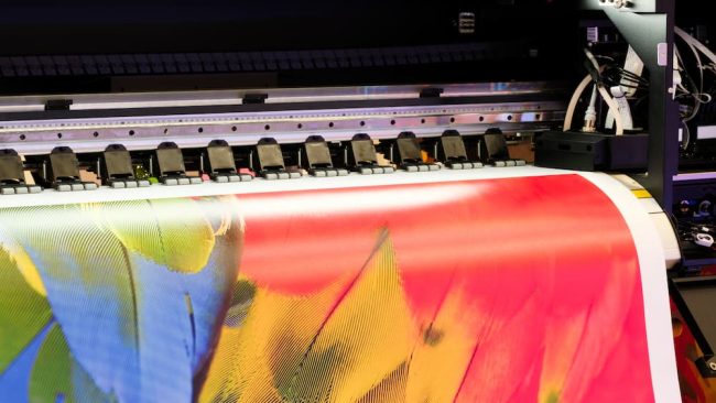 Close-up of a wide-format digital printer producing a vibrant color banner for printer support.