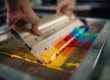 Close-up of a screen printing squeegee pulling colorful ink across a mesh frame, illustrating high-quality screen printing supplies and custom apparel techniques.